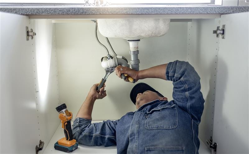 Plumber repairing pipes beneath a bathroom sink in Ocoee