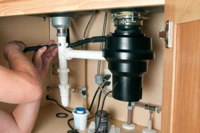 Plumber repairing a garbage disposal beneath a kitchen sink in Ocoee