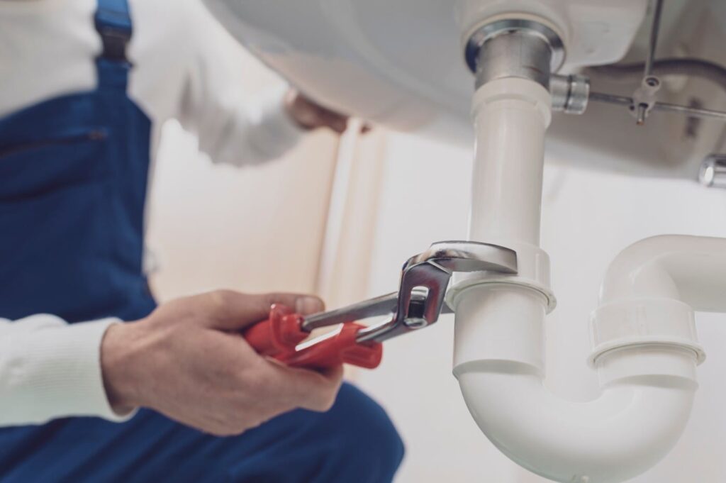Plumber repairing a white drain pipe beneath a sink in Ocoee